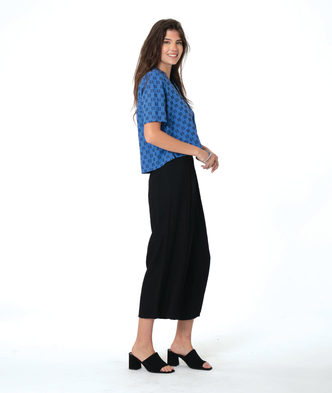 Woman wearing a blue and black checker board patterned top and black wide leg pants on a white background