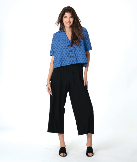 Woman wearing a blue and black checker board patterned top and black wide leg pants on a white background