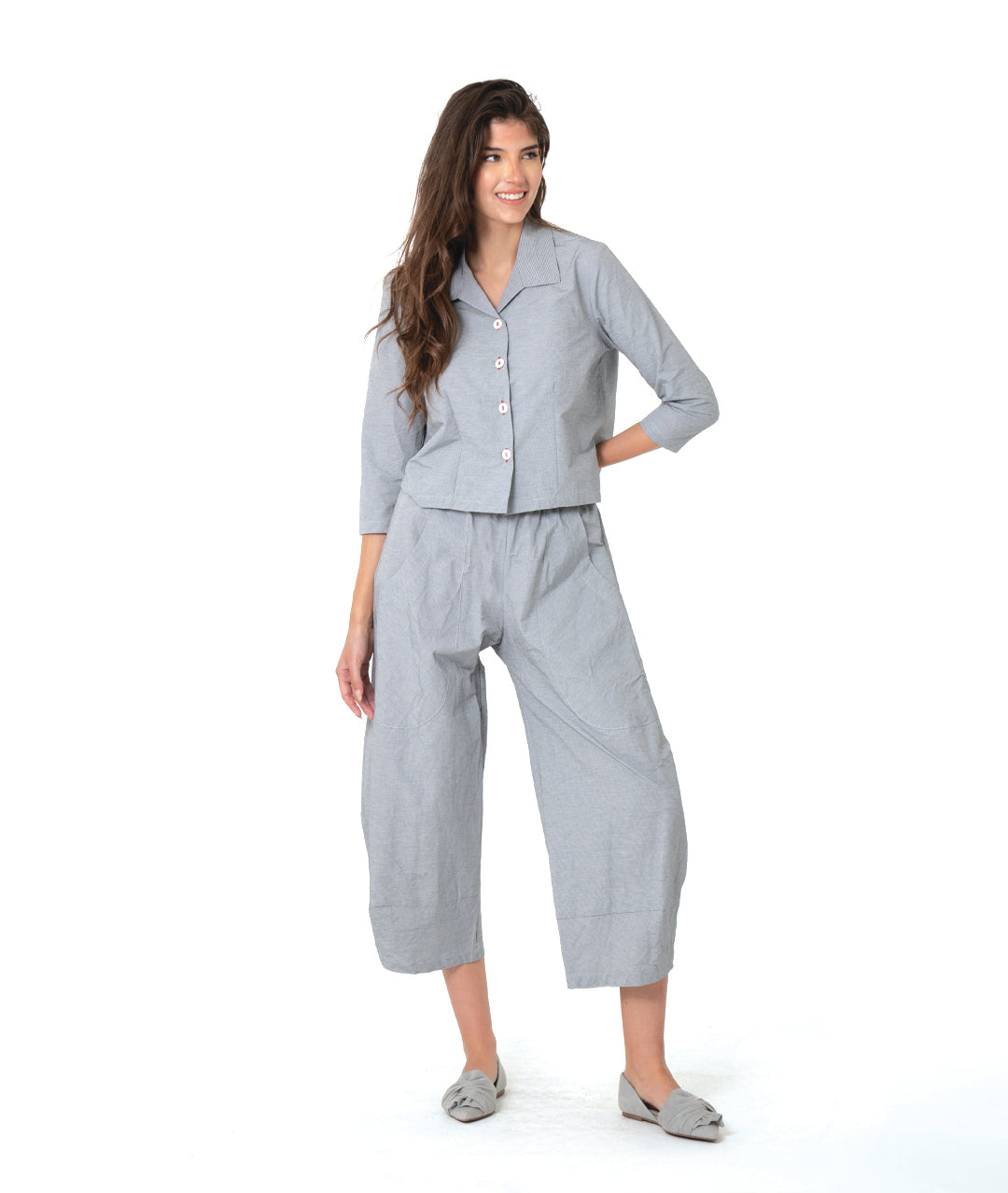 model in a grey and white pinstriped button down blouse with a short body, open collar, and contrasted red stitching at the buttons. worn with a matching wide leg pant