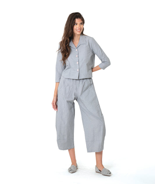 model in a grey and white pinstriped button down blouse with a short body, open collar, and contrasted red stitching at the buttons. worn with a matching wide leg pant
