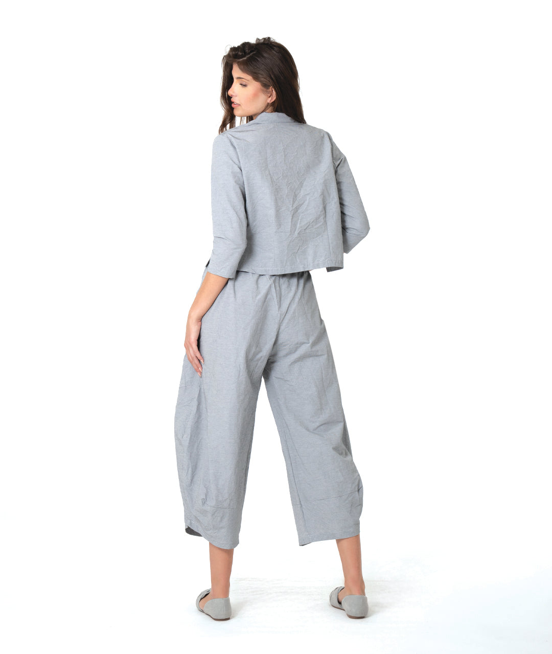 model in a grey and white pinstriped button down blouse with a short body, open collar, and contrasted red stitching at the buttons. worn with a matching wide leg pant