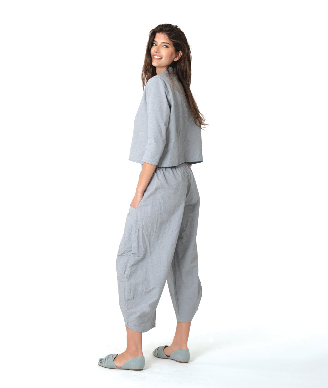 model in a grey and white pinstriped button down blouse with a short body, open collar, and contrasted red stitching at the buttons. worn with a matching wide leg pant