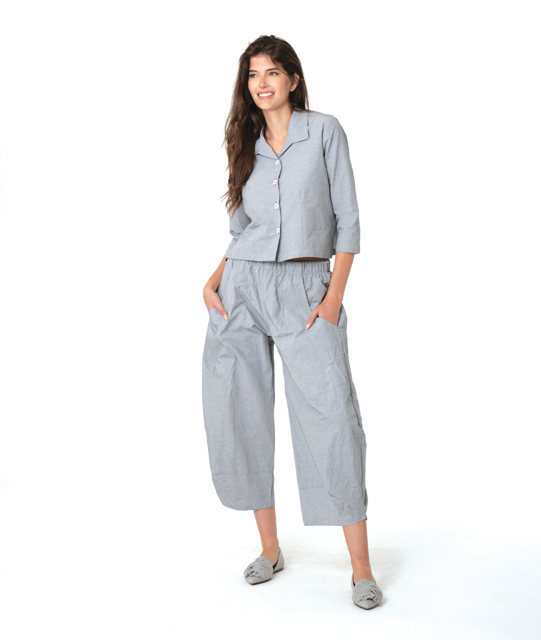 model in a grey and white pinstriped button down blouse with a short body, open collar, and contrasted red stitching at the buttons. worn with a matching wide leg pant