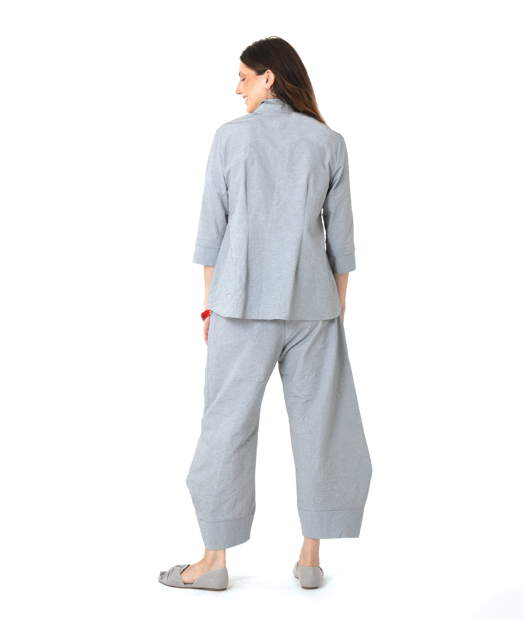 model in a grey and white pinstriped button down blouse with a double collar, oversized cuffs, and contrasted red stitching at the buttons. worn with a matching wide leg pant