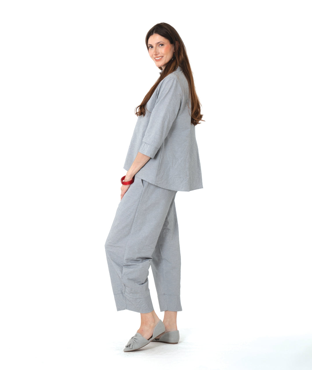 model in a grey and white pinstriped button down blouse with a double collar, oversized cuffs, and contrasted red stitching at the buttons. worn with a matching wide leg pant