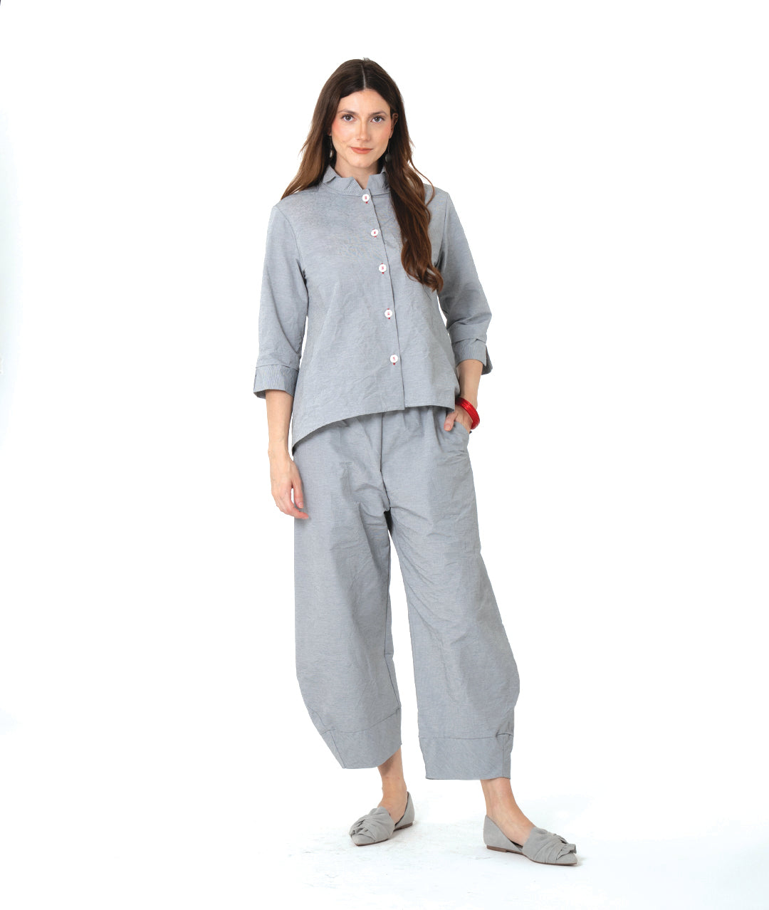 model in a grey and white pinstriped button down blouse with a double collar, oversized cuffs, and contrasted red stitching at the buttons. worn with a matching wide leg pant