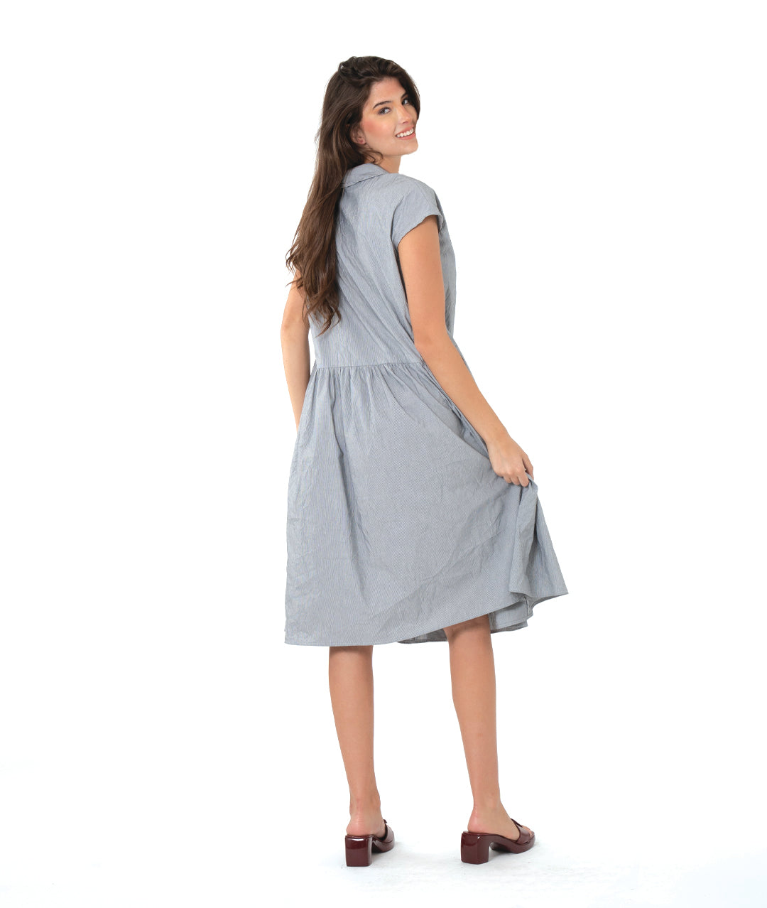 model in a grey and white pinstriped button down dress with a dropped waist, cap sleeves, squared hip pockets and contrasted red stitching at the buttons.