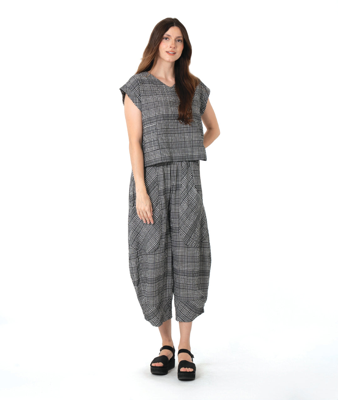 model in a black, white and grey plaid pair of pants with oversized contrasting pockets, wide legs and a tapered ankle. worn with a matching boxy pullover top