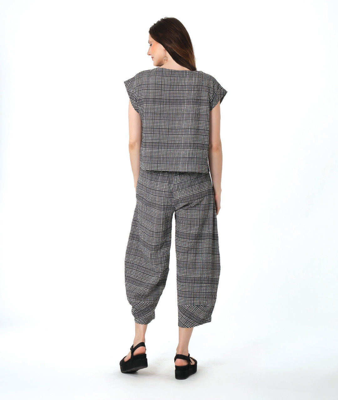 model in a black, white and grey plaid pair of pants with oversized contrasting pockets, wide legs and a tapered ankle. worn with a matching boxy pullover top