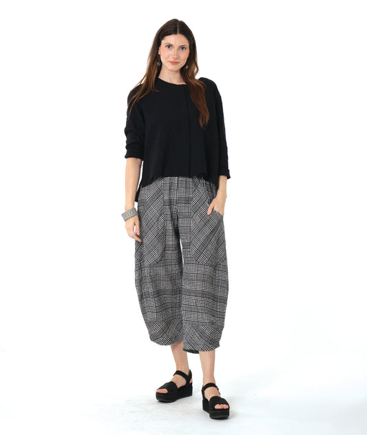 model in a black pullover top with a false placket and a hi-low hem, worn with a grey plaid pant