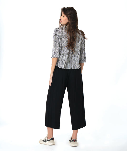 model in a wide leg black pant with a split at the ankle front, worn with a black and white striped blouse with 3/4 sleeves and a twin button detail