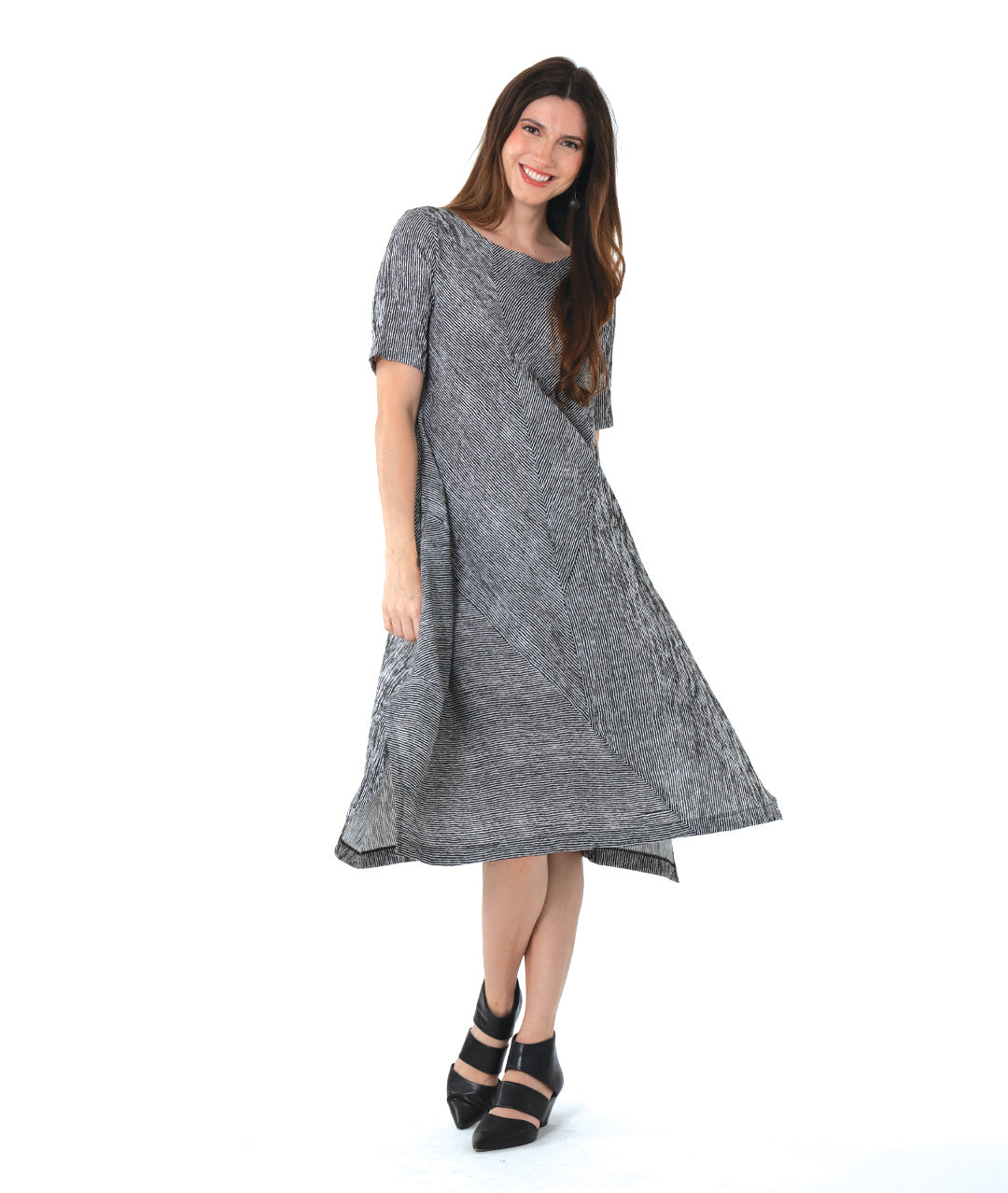 model in a black and white striped dress with contrasting panels of directional stripes. Dress has a round neckline, elbow length sleeves and splits and tucks at the sides