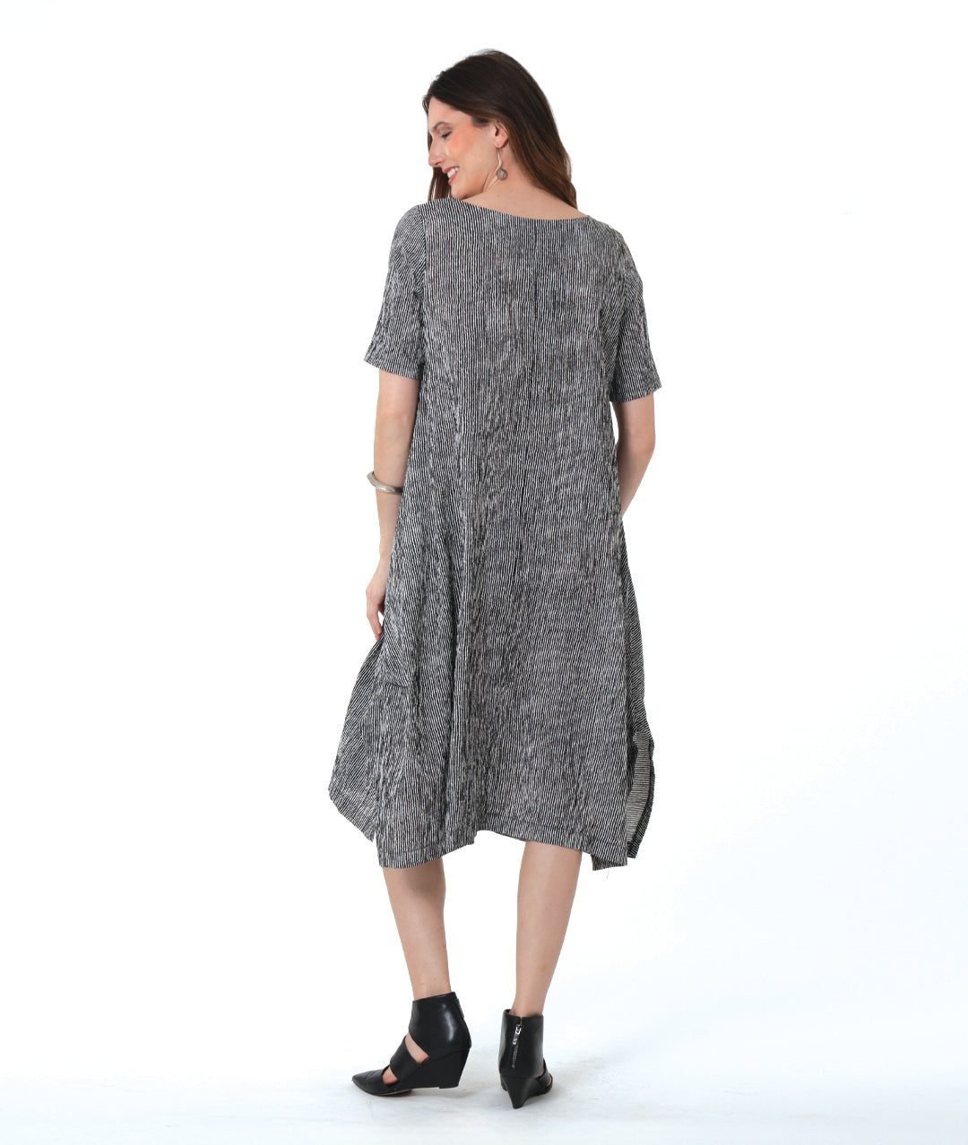 model in a black and white striped dress with contrasting panels of directional stripes. Dress has a round neckline, elbow length sleeves and splits and tucks at the sides