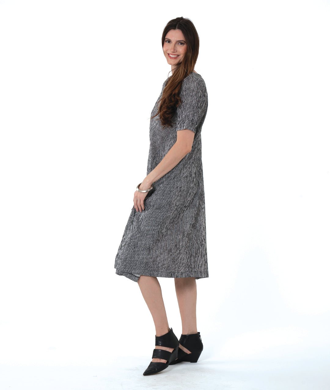 model in a black and white striped dress with contrasting panels of directional stripes. Dress has a round neckline, elbow length sleeves and splits and tucks at the sides