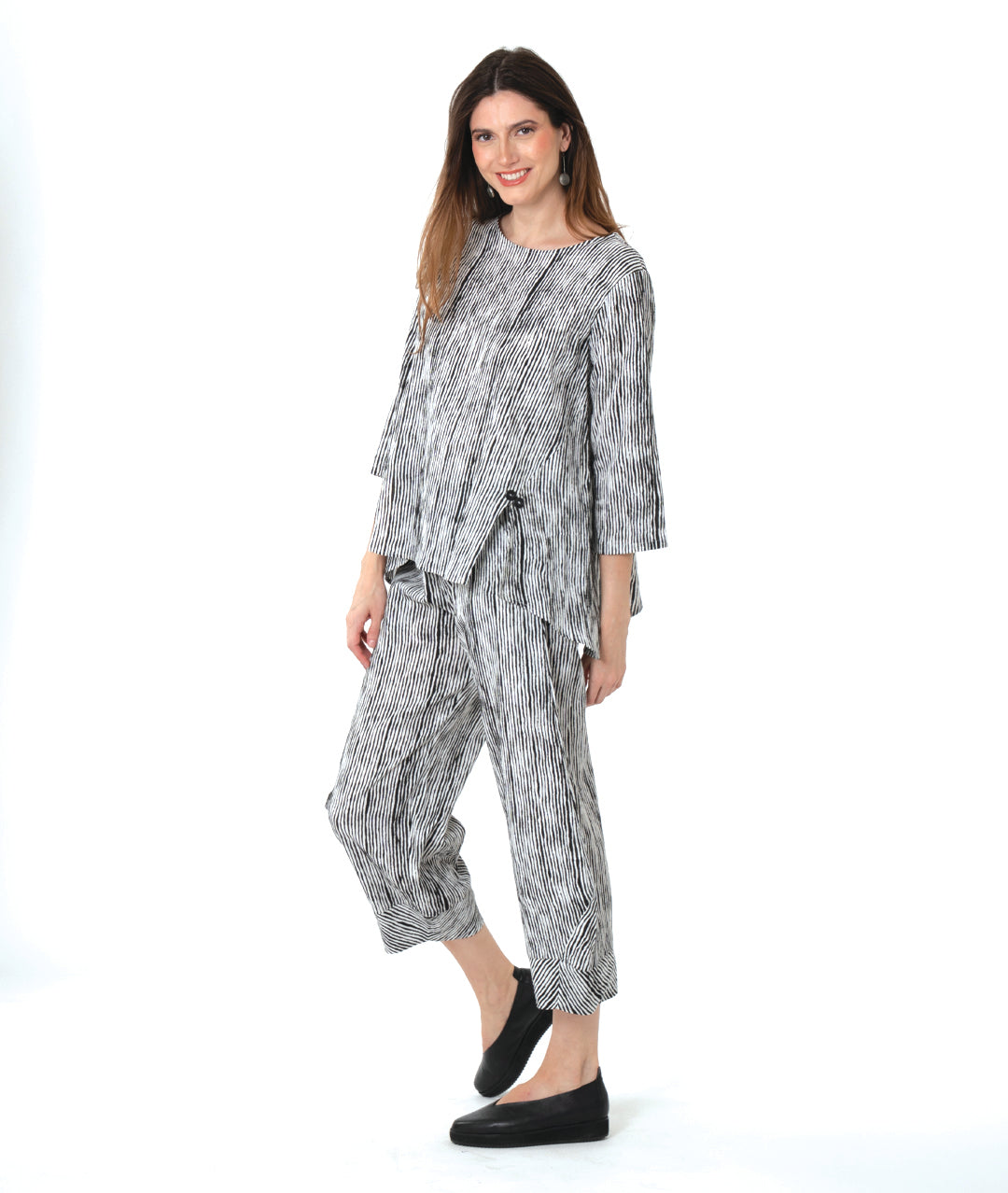 model in a wide leg black and white striped pant with a tapered ankle, worn with a matching pullover blouse with front splits and a double button detail
