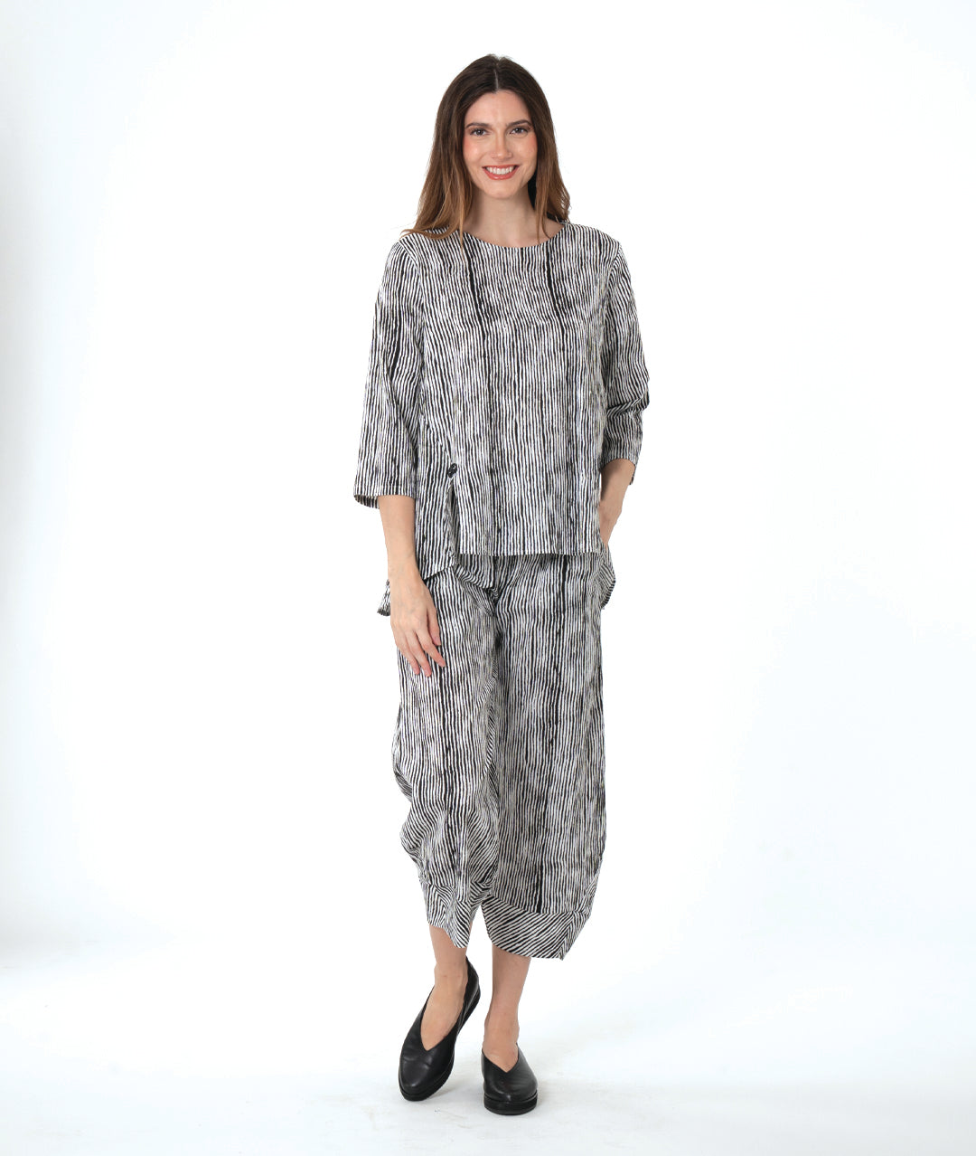 model in a wide leg black and white striped pant with a tapered ankle, worn with a matching pullover blouse with front splits and a double button detail