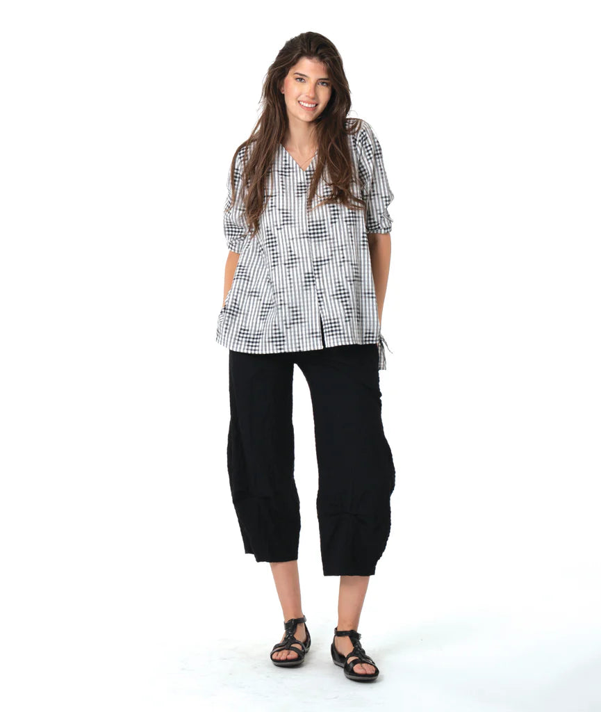 Woman wearing a black and white patterned shirt and black pants on a white background