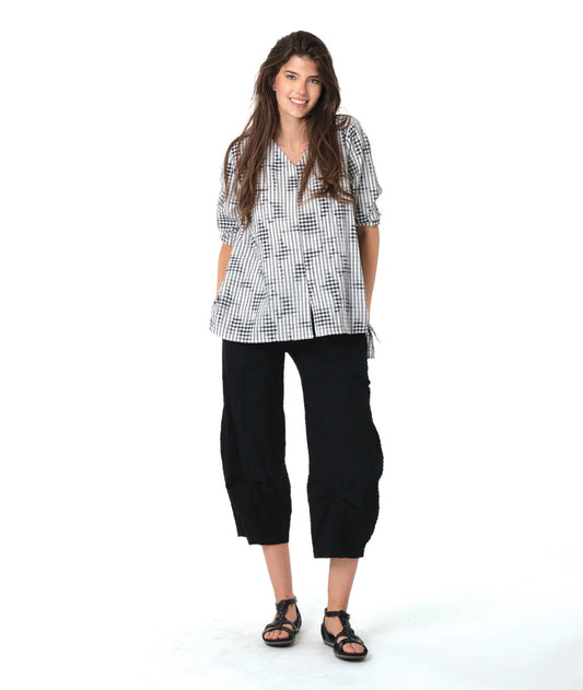 Woman wearing a black and white patterned shirt and black pants on a white background