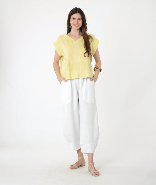 A woman modeling a light yellow short-sleeve linen top and white wide-leg linen pants against a plain white studio background.