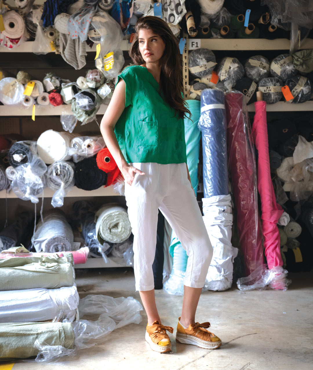 model in a fabric warehouse in a white cropped pant and a boxy green pullover top