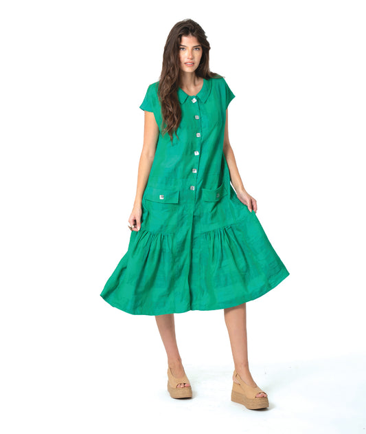 A woman modeling a bright green short-sleeve midi dress with a button-down front, tiered skirt, and front pockets, paired with tan wedge sandals, against a plain white studio background.