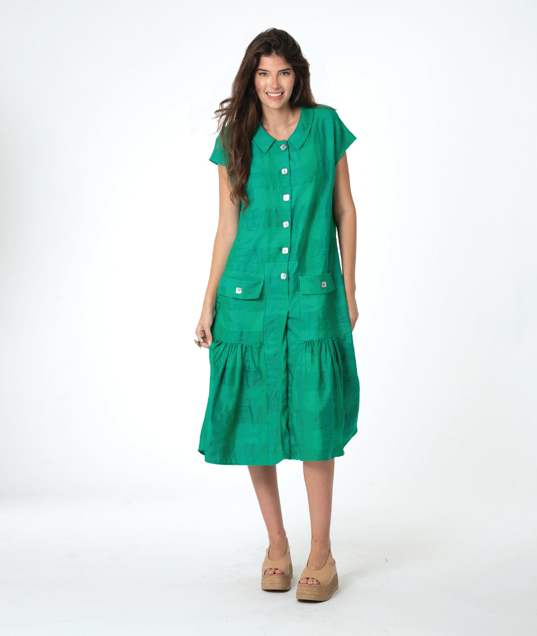 A woman modeling a bright green short-sleeve midi dress with a button-down front, tiered skirt, and front pockets, paired with tan wedge sandals, against a plain white studio background.