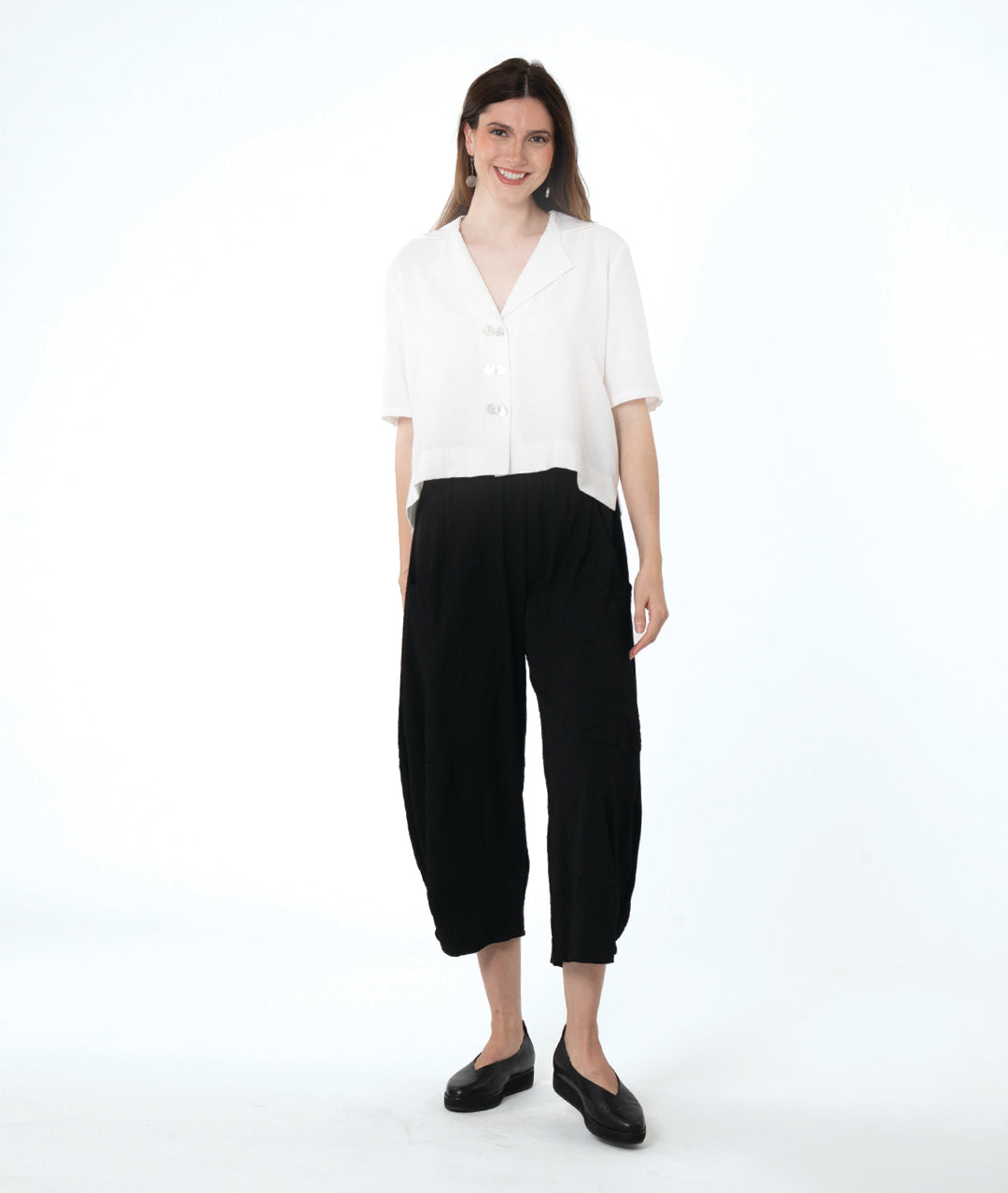 model in a cropped black pant with a boxy button down with an elbow length sleeve and an open collar