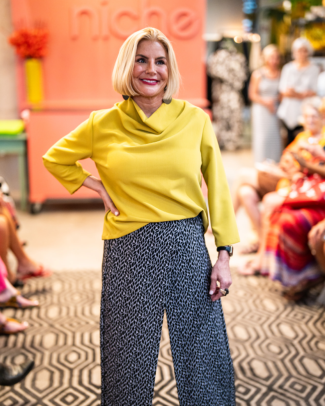 model posing for people wearing a yellow cowl top with 3/4 sleeves and wide leg black and grey leaf print pant with an overlapping front