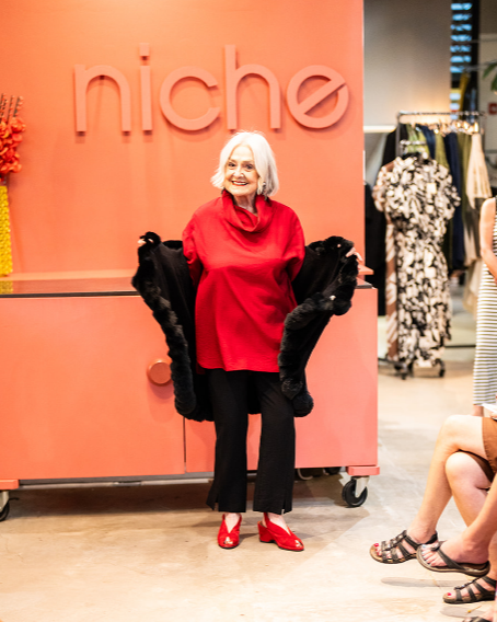 model walking down runway wearing red cowl top with black fur coverup, black pants and red shoes