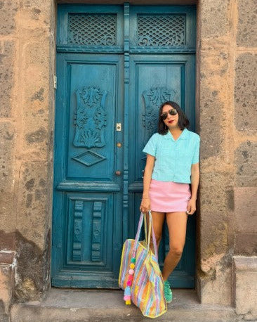 Woman standing in front of door wearing turquoise shirt and pink skirt