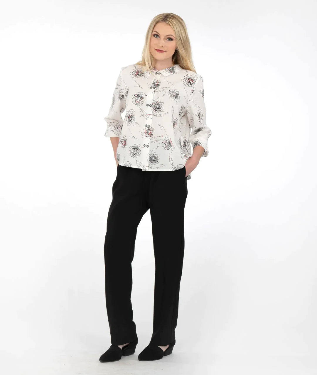 model in a white buttoned blouse with a red and black rose print, worn with black pants 