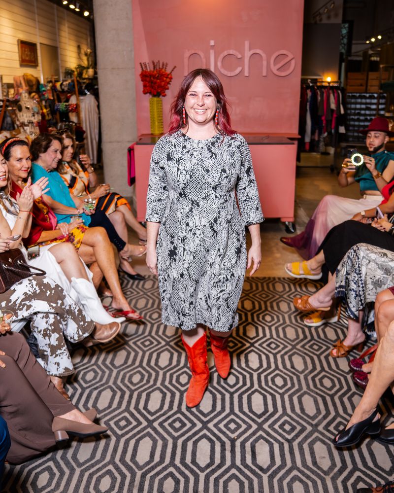 model in a patterned black and white dress and red boots walking down runway