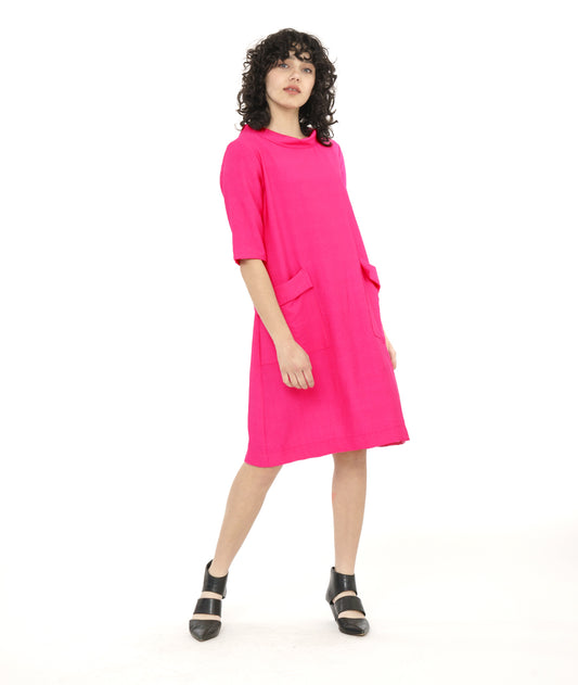 model in a hot pink knee length shift dress with elbow length sleeves, a round cowl neck collar and exterior hip pockets