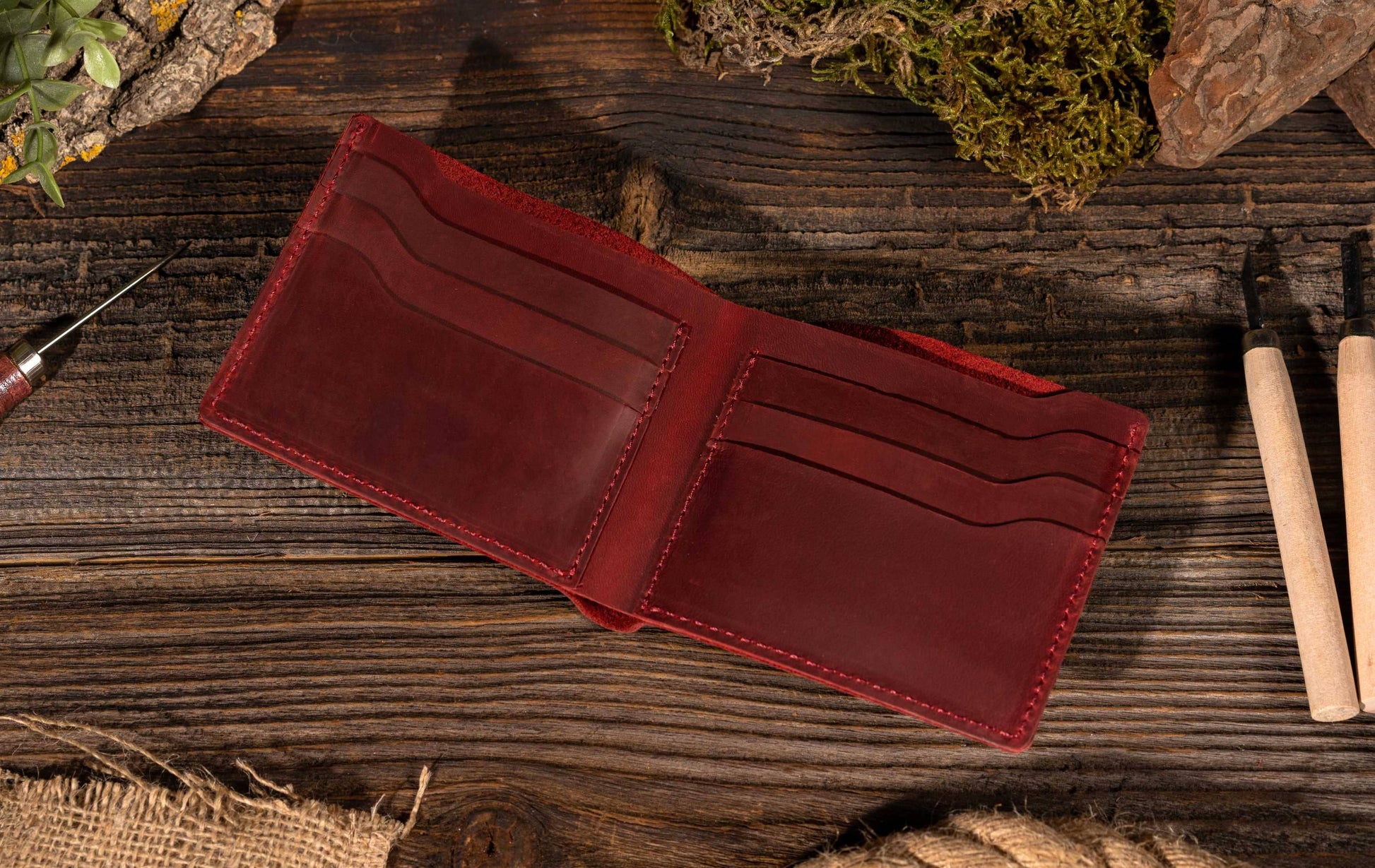 red leather wallet opened on top of wood surface with tools, rocks and greenery surrounding it