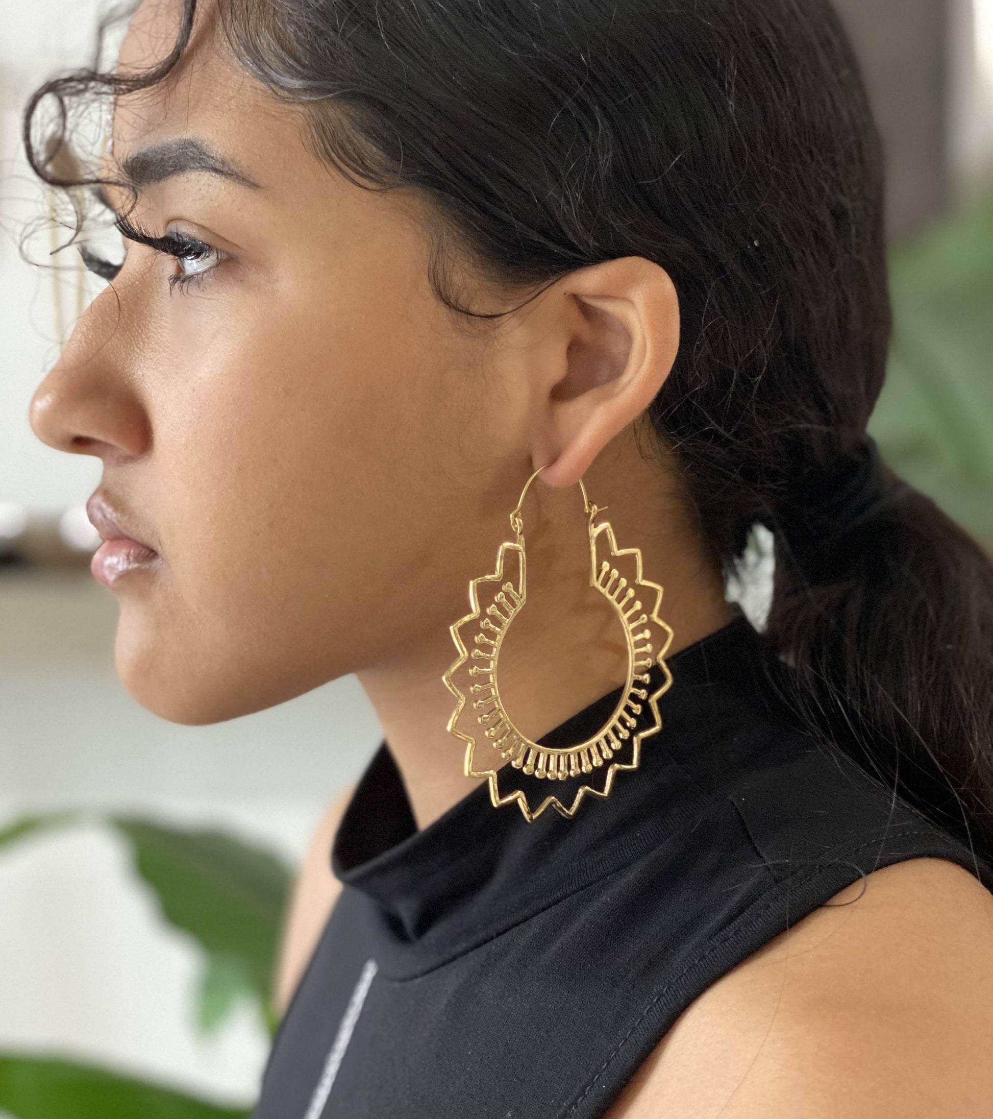 Hoop earrings with ridges and stick designs on a model with dark hair wearing a sleeveless mock neck black top.