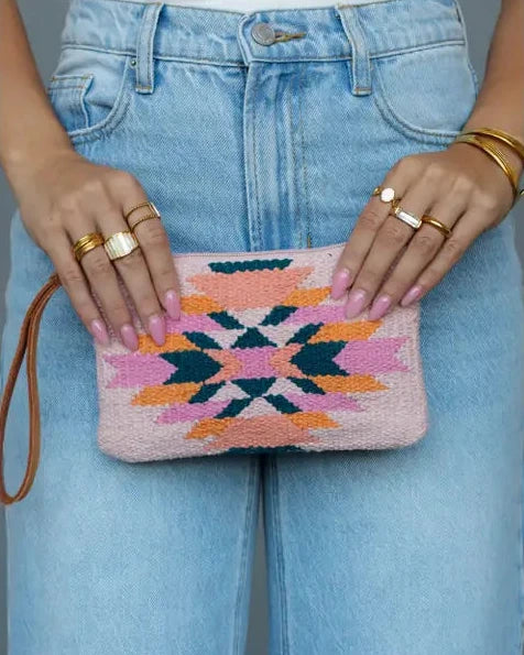 Person holding a colorful patterned clutch with denim jeans and gold rings.