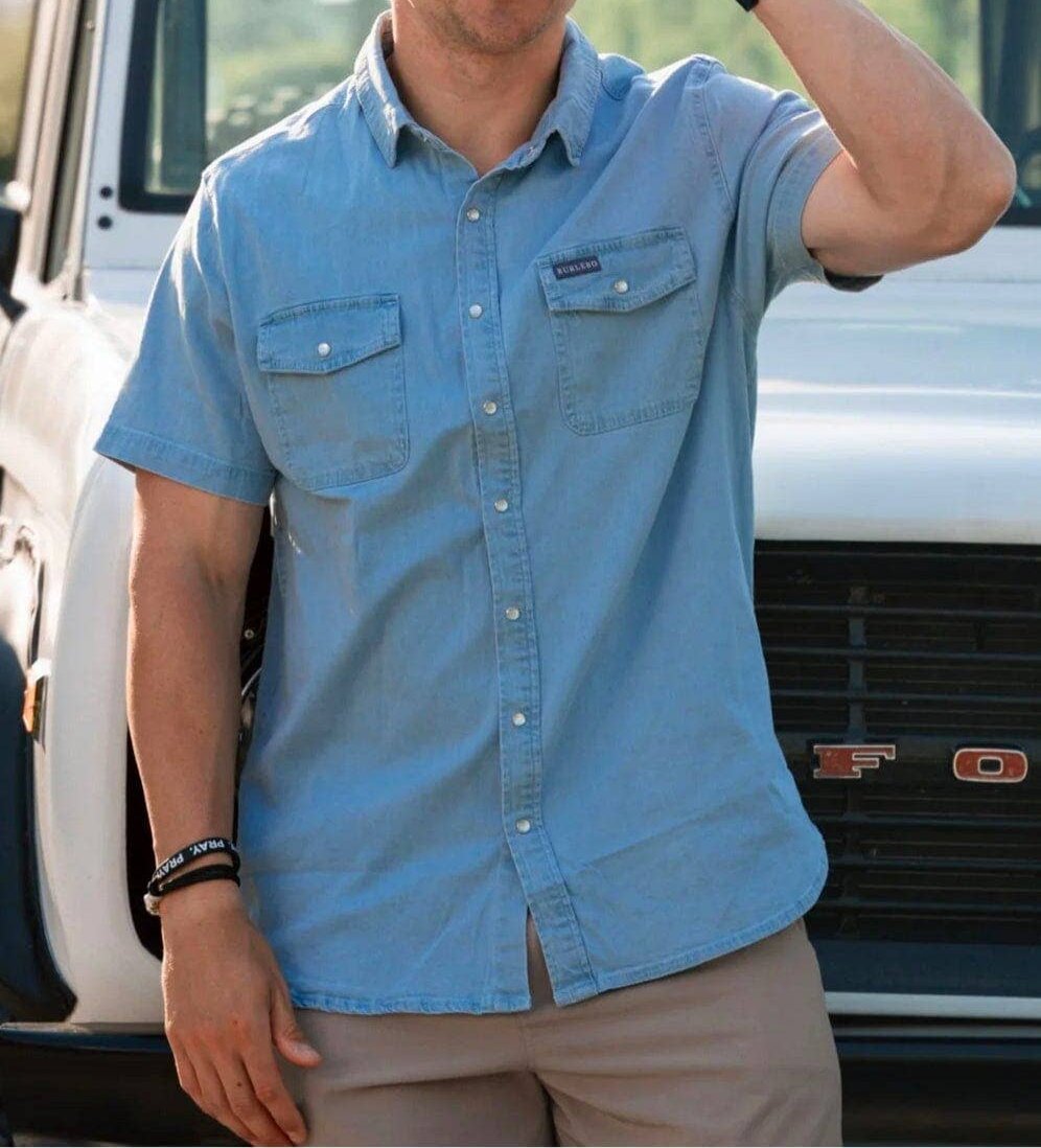 male model wearing short sleeve light blue denim pearl snap shirt in front of a white ford bronco