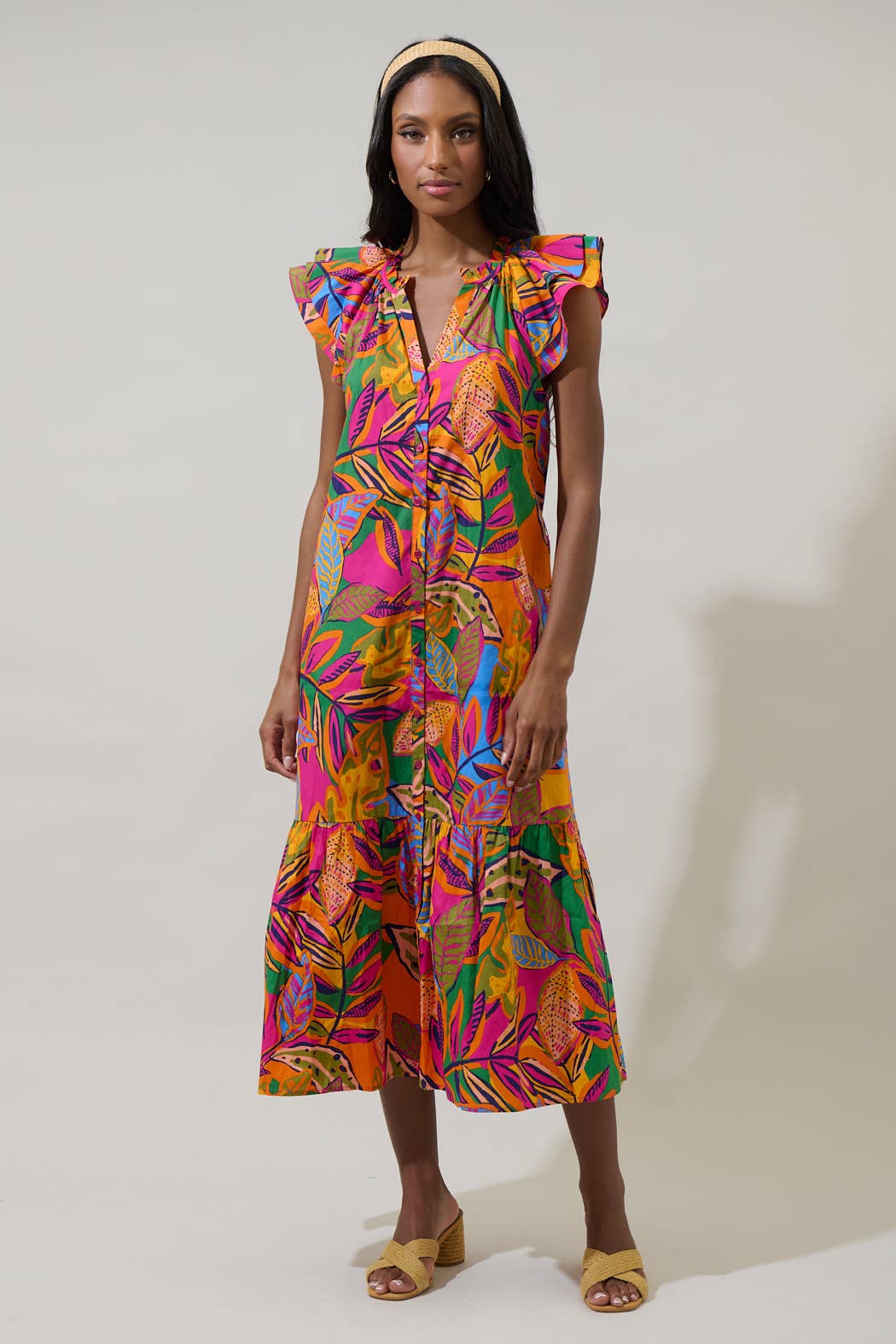 model in a midi length tropical print dress with a ruffled neckline and buttons at the center front