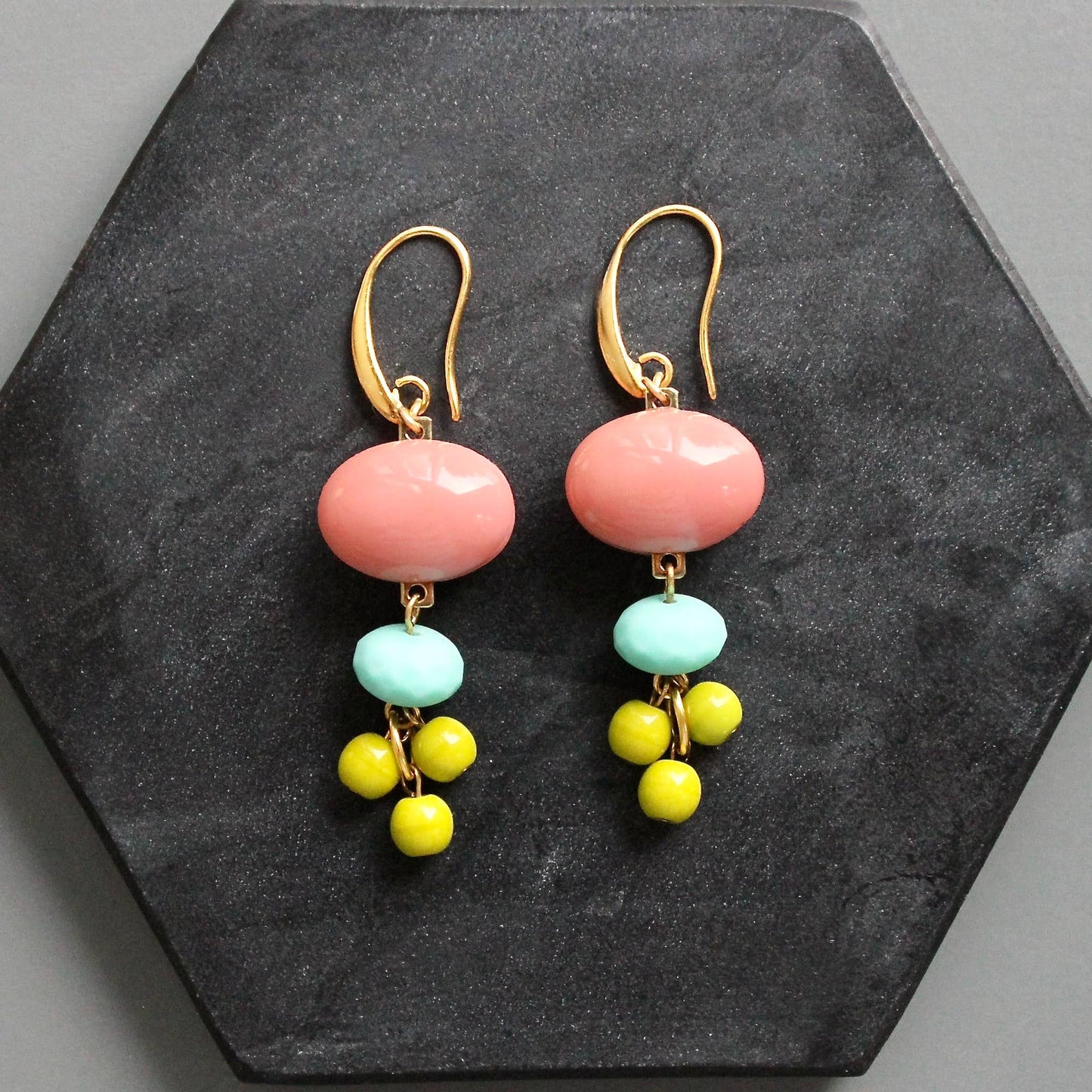 Pair of earrings with pink, turquoise, and yellow beads on a dark stone surface