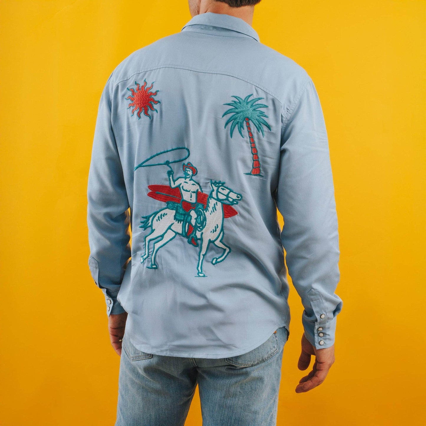 Person wearing a light blue denim shirt with colorful graphics on the back against a yellow background