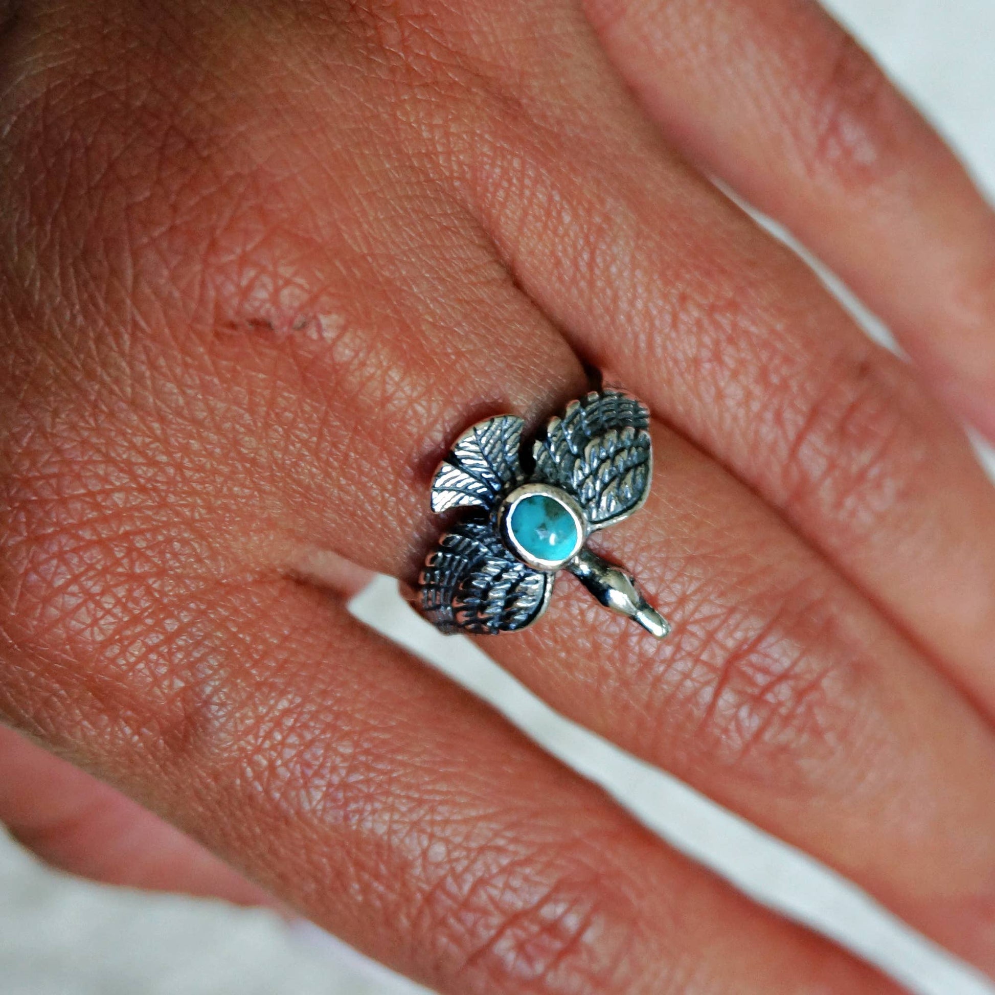 Silver ring with a blue gemstone on a person's finger
