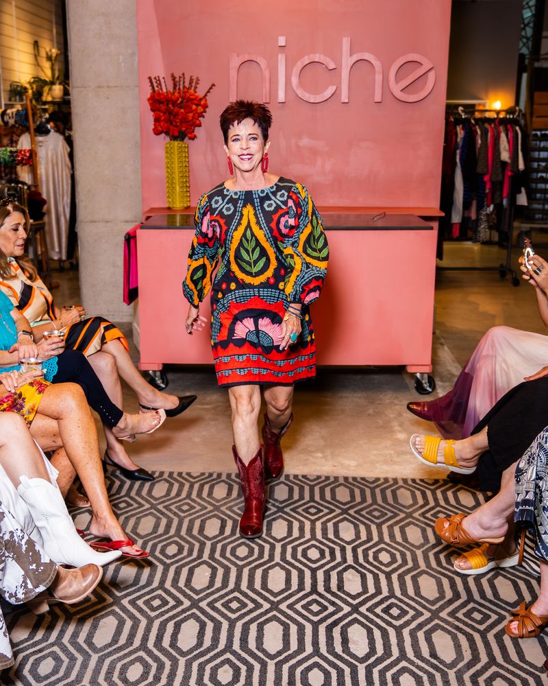 model in a colorful embroidered dress and red boots walking down runway