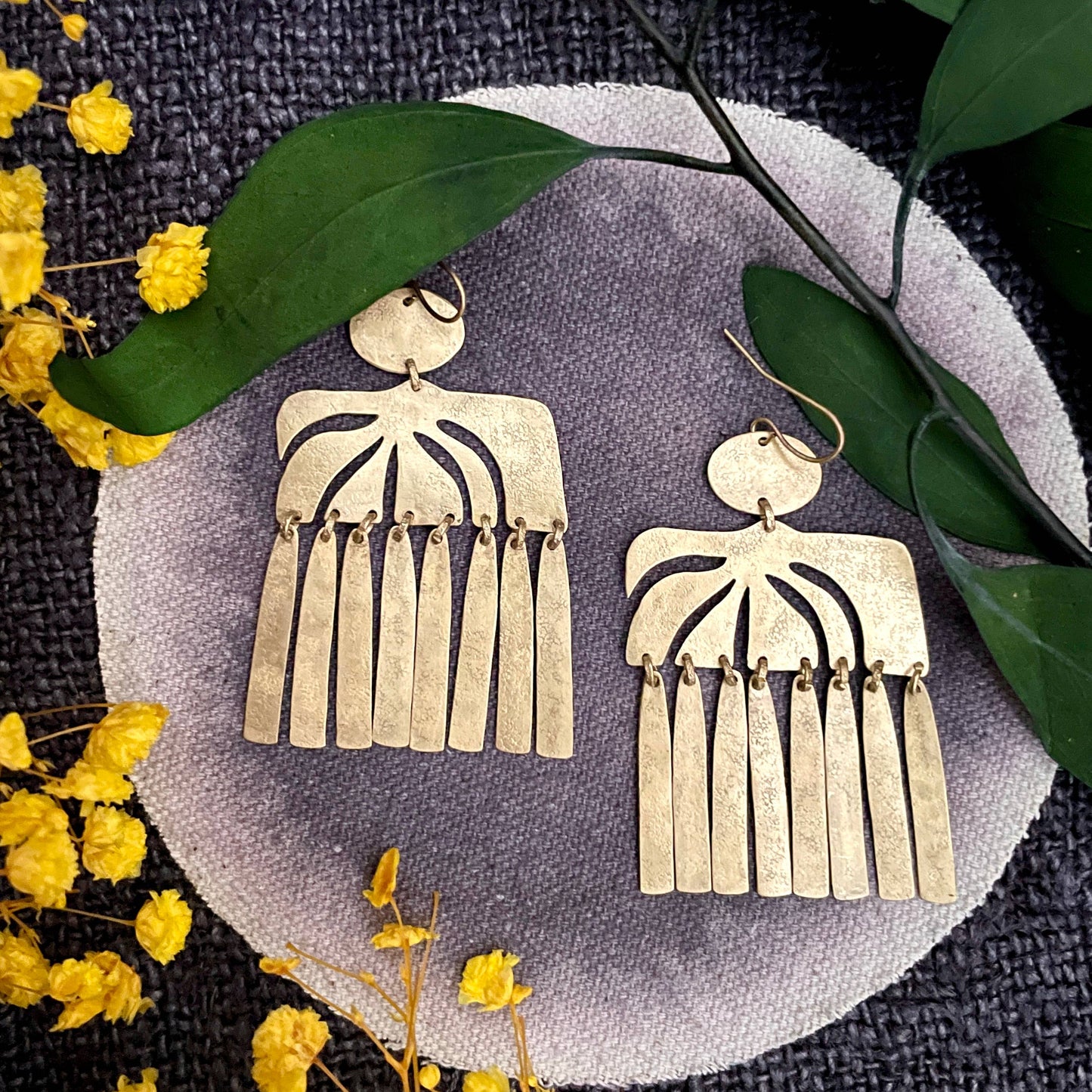 Gold fringe earrings on a round gray stone with yellow flowers and green leaves.
