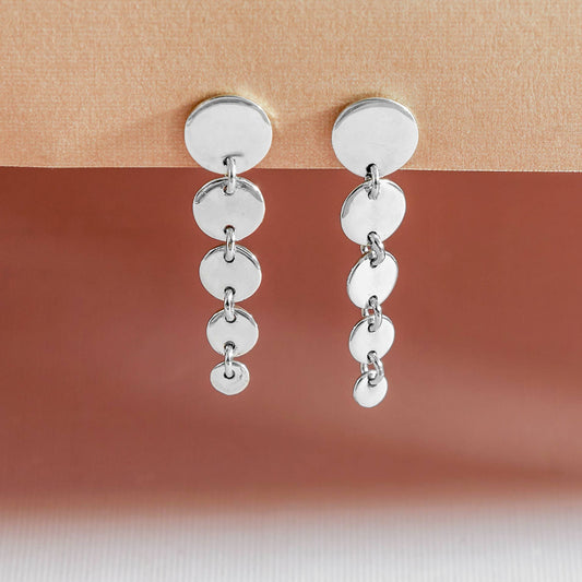 A pair of sterling silver cascading circle post earrings displayed against a beige background.