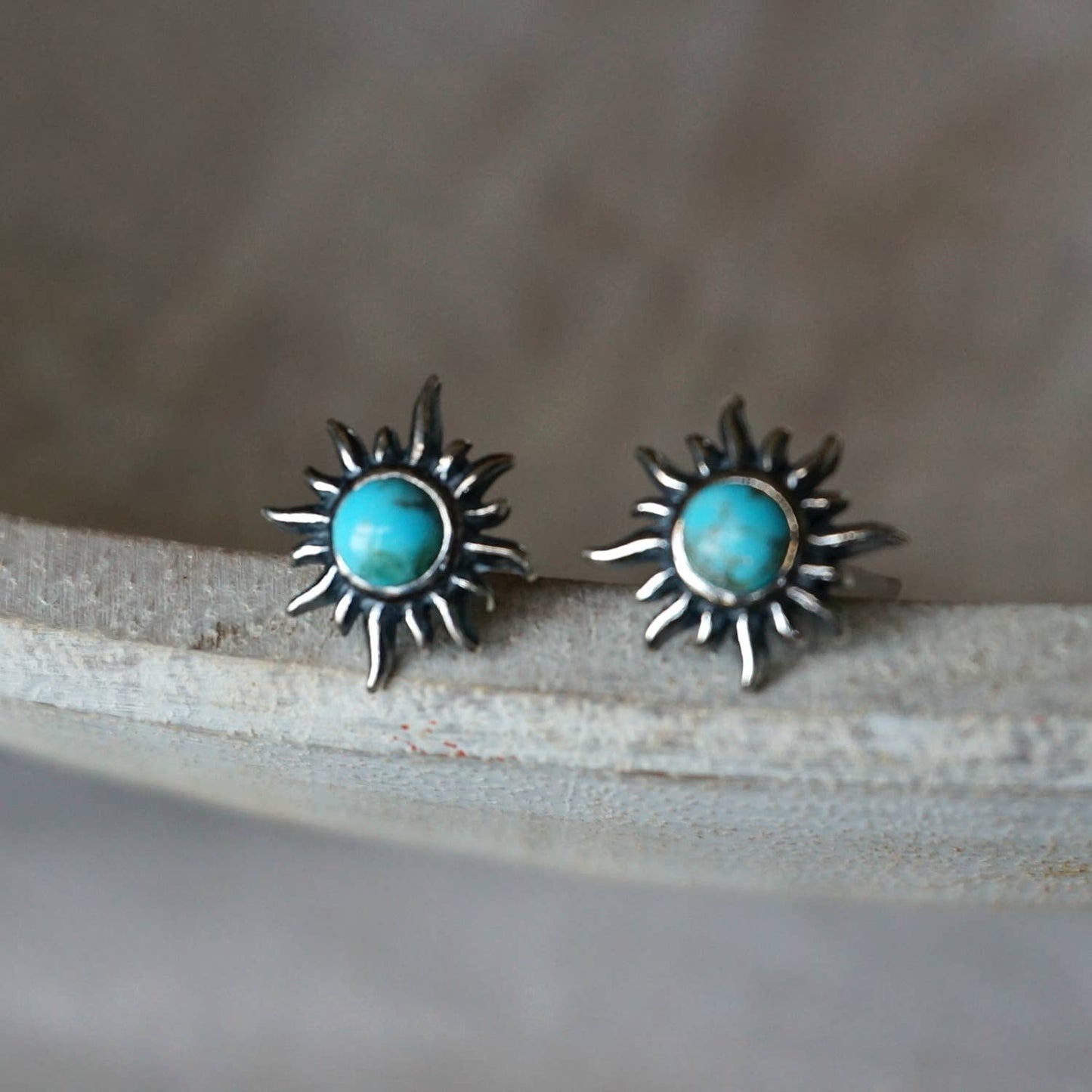 Sun-shaped earrings with turquoise stones on a textured surface