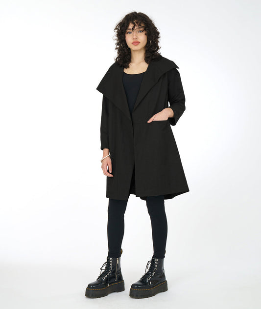 model in a black legging and top, worn with a black jacket with an oversized collar and asymmetrical pocket detail