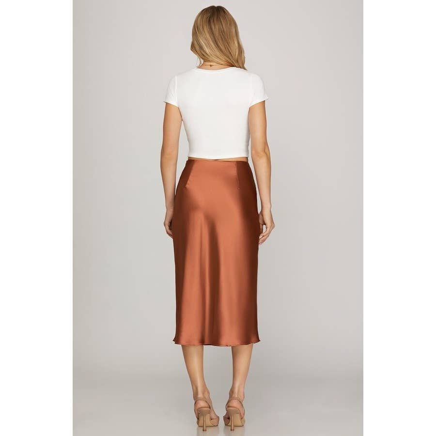 Woman wearing a white top and copper satin skirt on a plain background