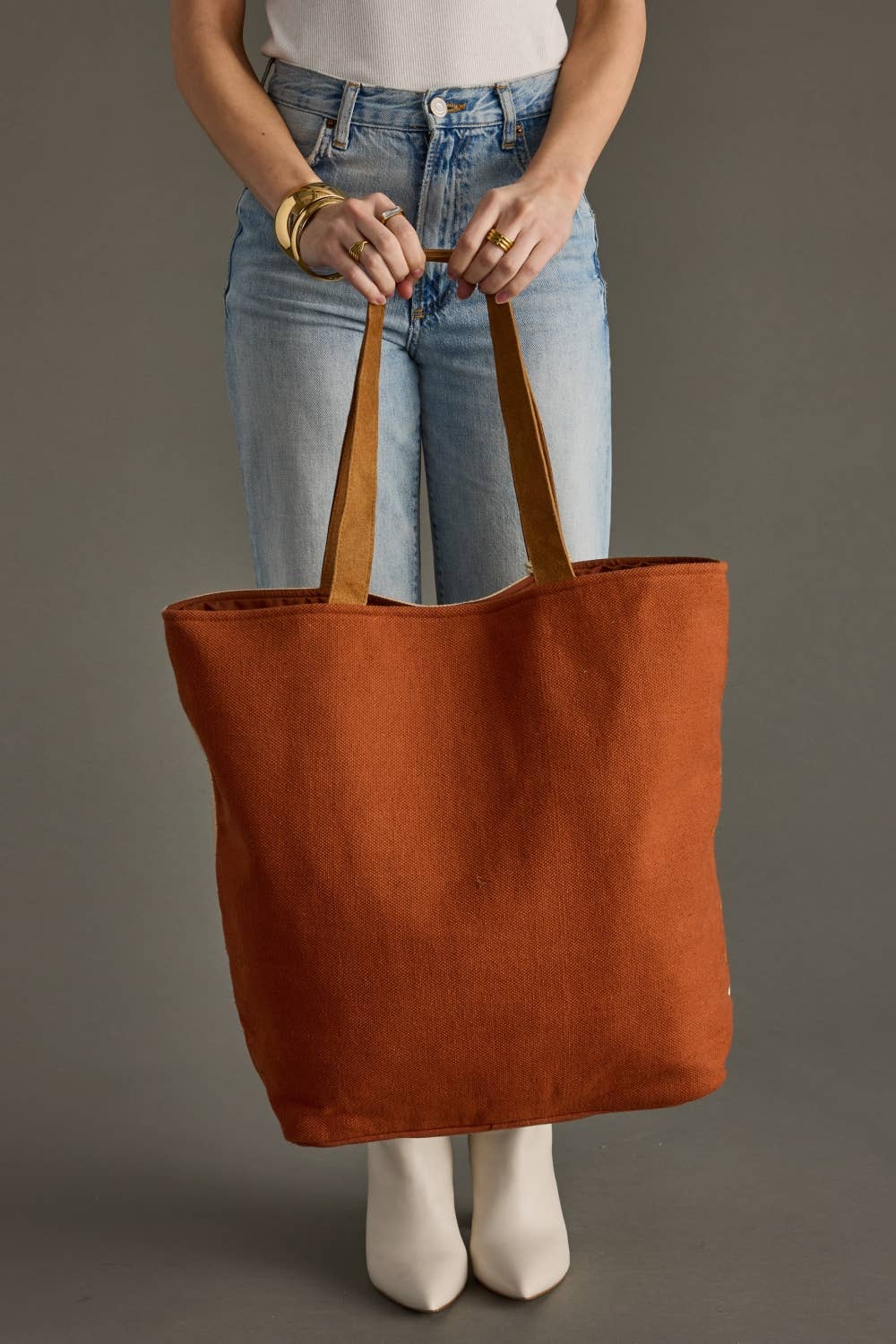 Person holding a brown tote bag against a gray background
