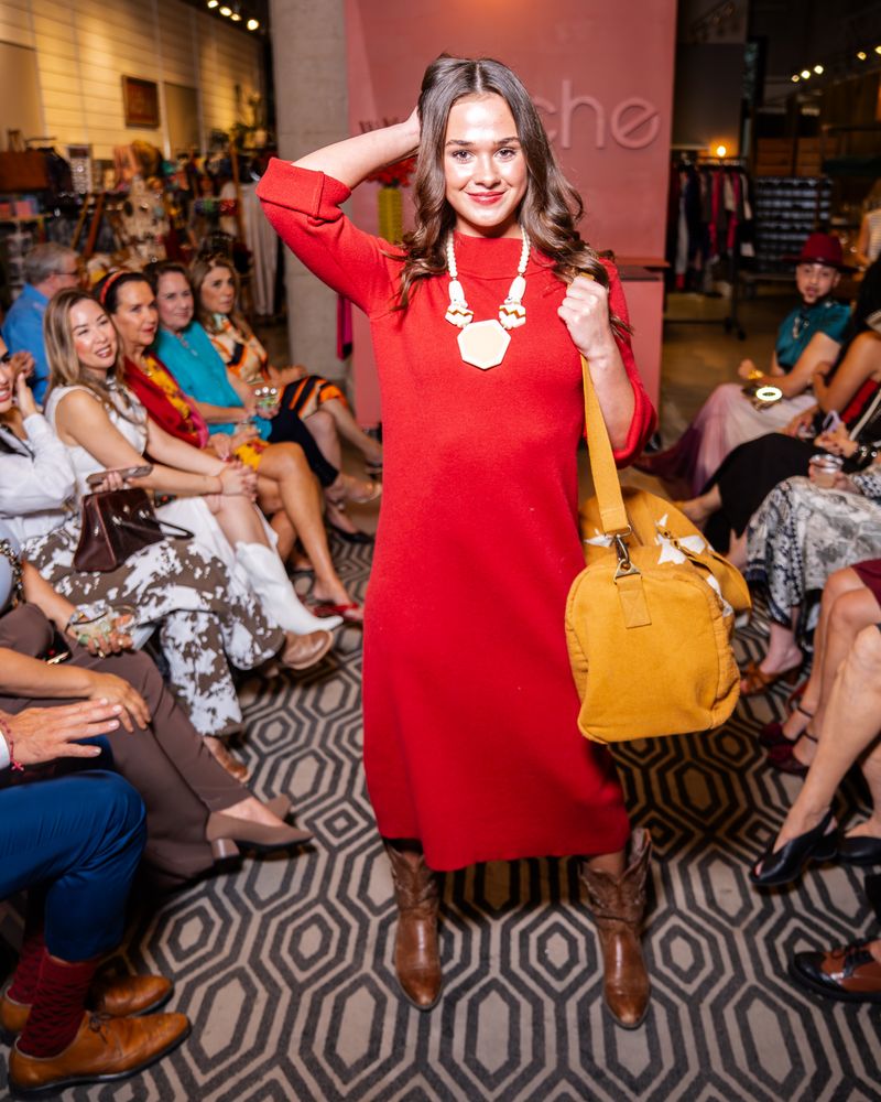 model wearing a red dress, chunky necklace and cowboy boots holding a yellow bag on a runway