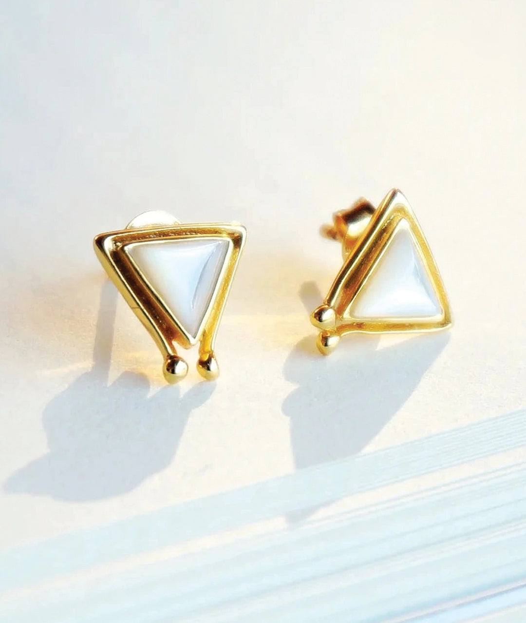 Gold triangle-shaped earrings on a light background